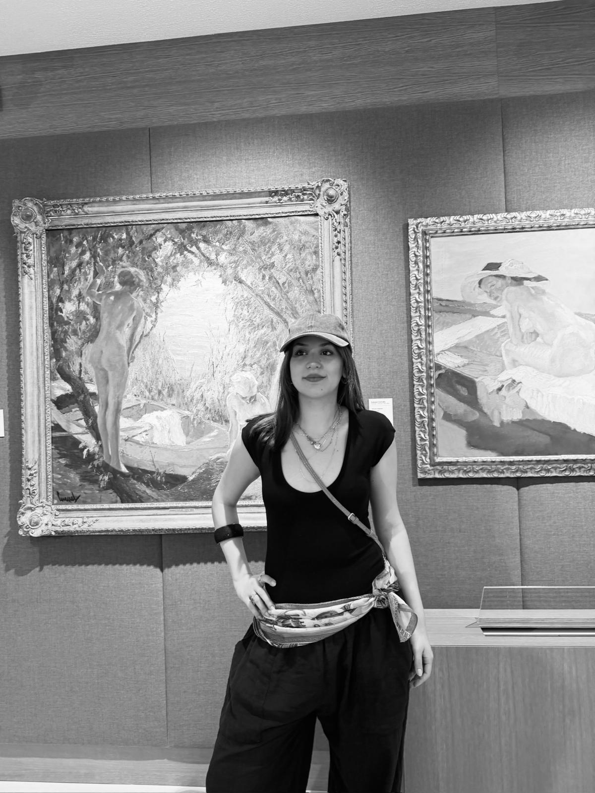 Azra Vardar standing in front of paintings in a gallery.